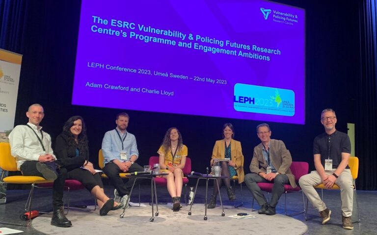 Members of the Vulnerability & Policing Futures Research Centre sat on chairs on a stage with presentation slides on a large screen behind them