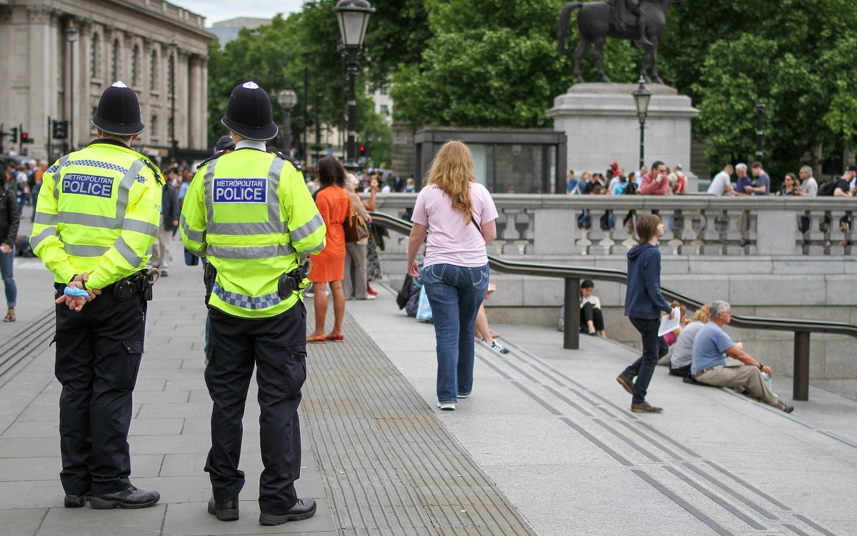 Two Metropolitan police officers stood at Trafalgar Square as members of the public walk by