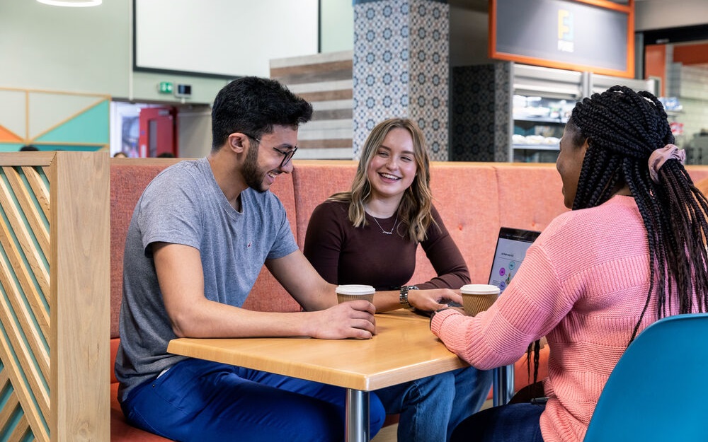 A group of young people sat at a cafe smiling and chatting