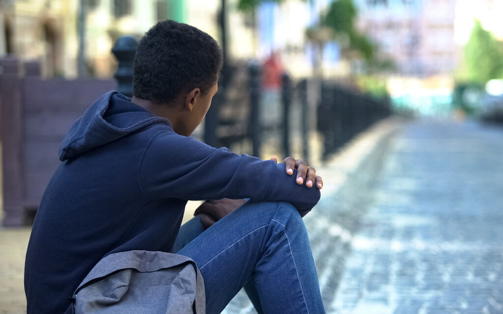 Teenager with backpack sat on the pavement of an empty street